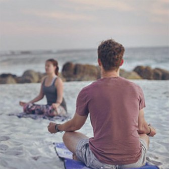 Man and woman doing yoga on the beach